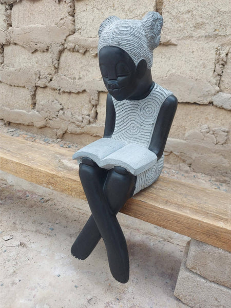 stenen beeld van een meisje dat een boek leest, gekruiste benen