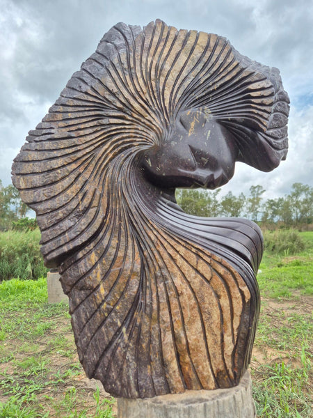 stenen beeld van Lovemore Bonjisi, mooie kleuren, bruin en auberginekleur, uniek stuk, meisje met grote haardos, typische stijl van Bonjisi, tuinbeelden